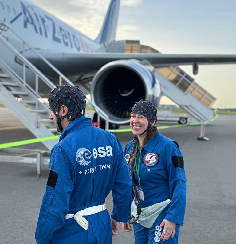 Two members of an ESA team in EEG caps in front of an aircraft