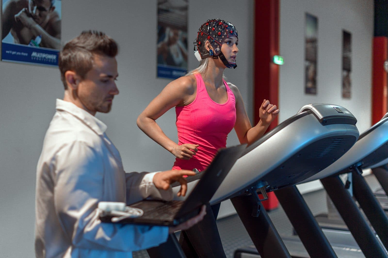 A participant running on a treadmill in an EEG cap, watched by a researcher with a laptop