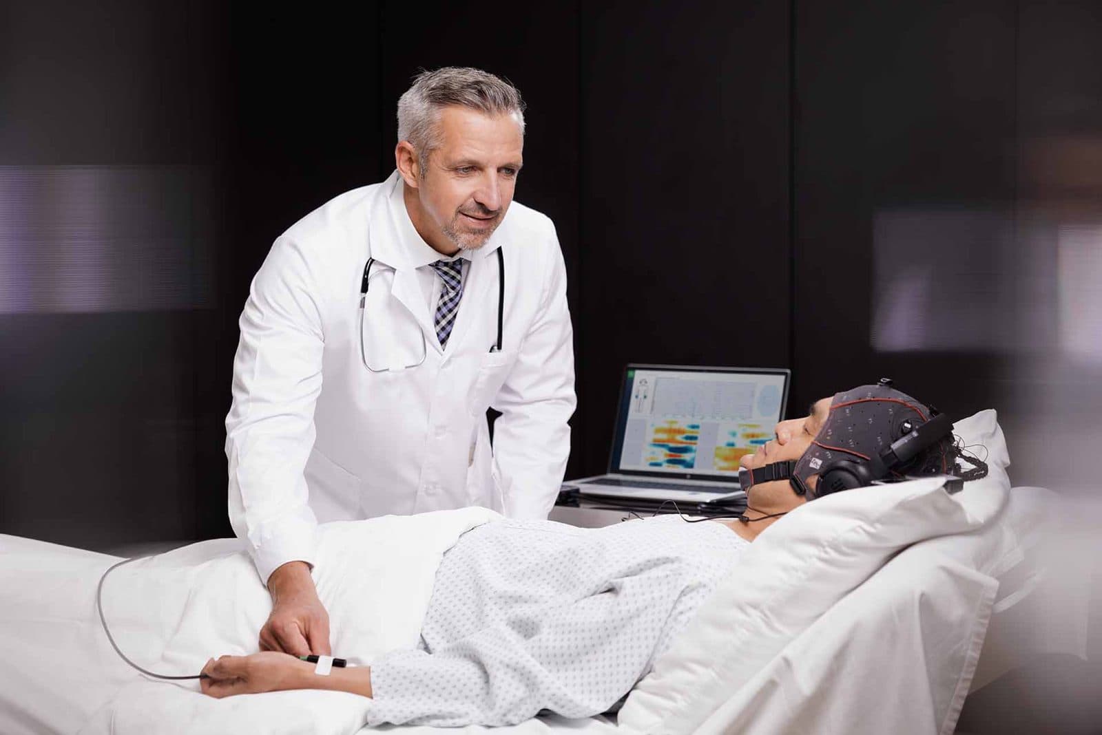 A patient lying in bed in an EEG cap with a doctor beside him