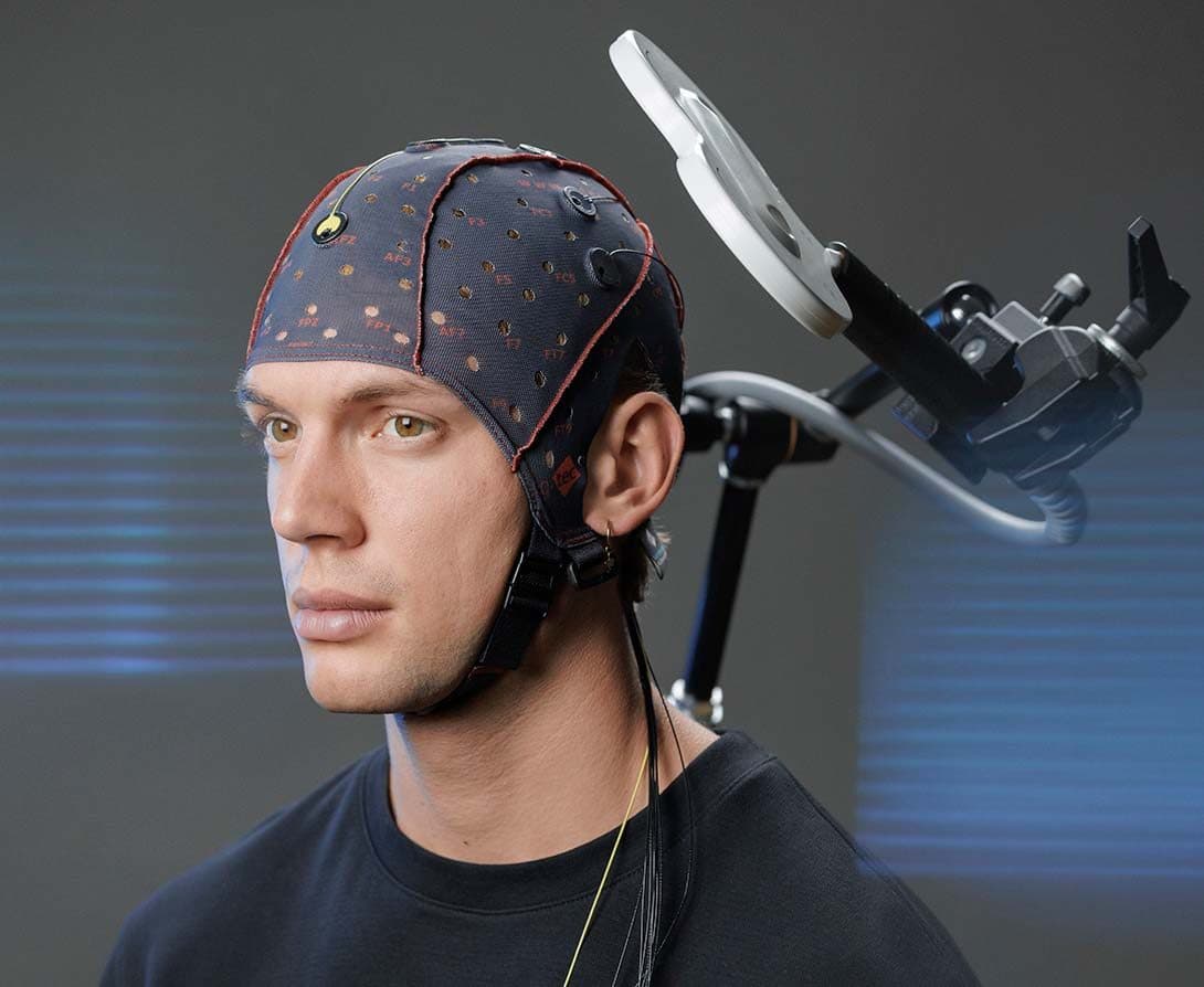 A TMS coil at the head of a participant wearing an EEG cap