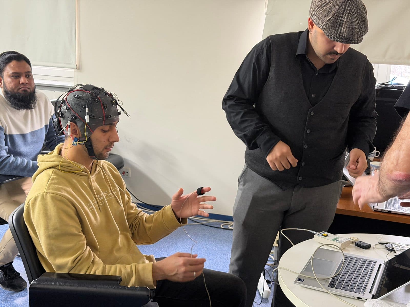 A participant wearing an EEG cap and a finger sensor watches the recording with the students around them.