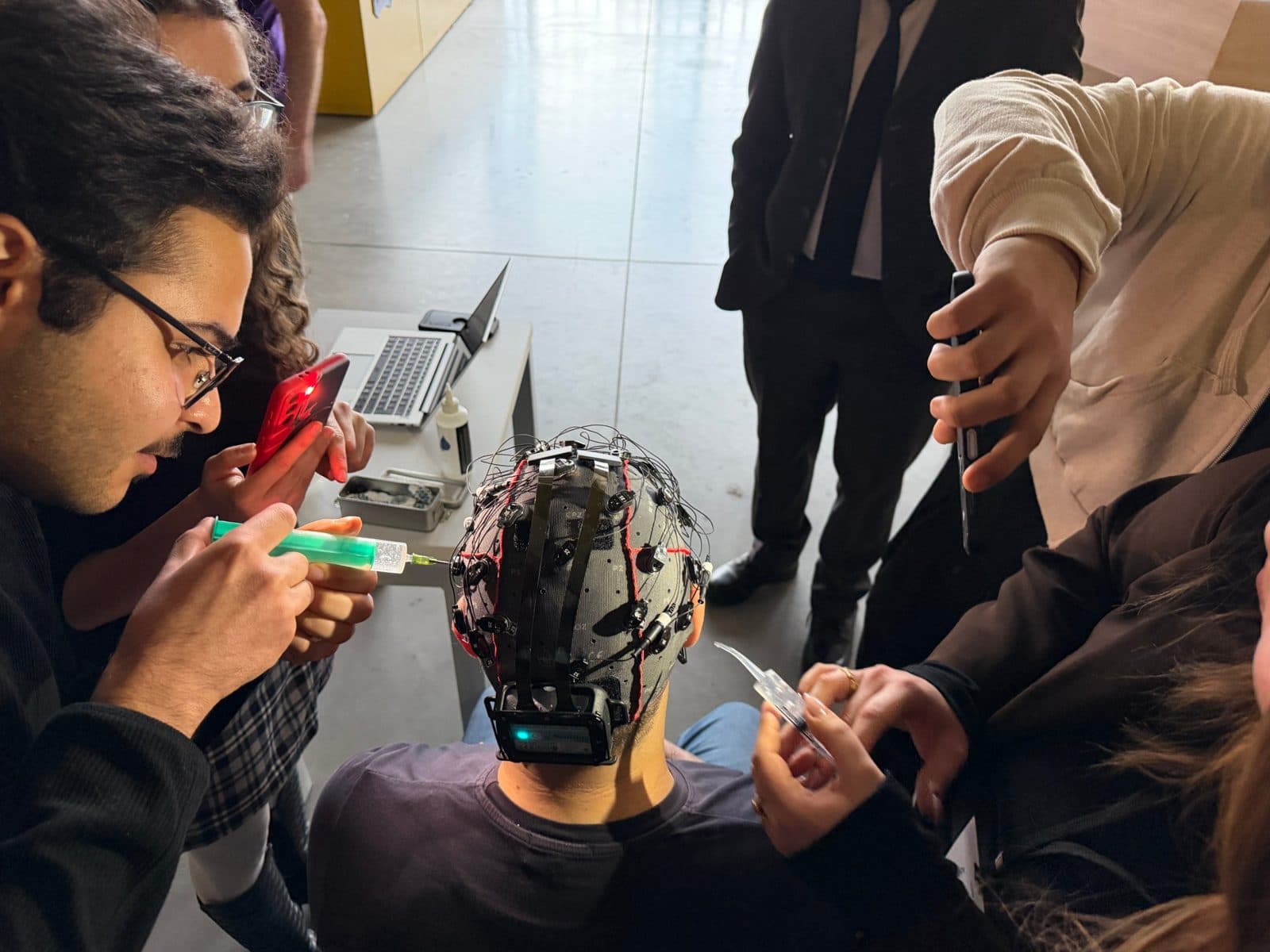 Students apply gel with a syringe to the electrodes of an EEG cap worn by a participant.
