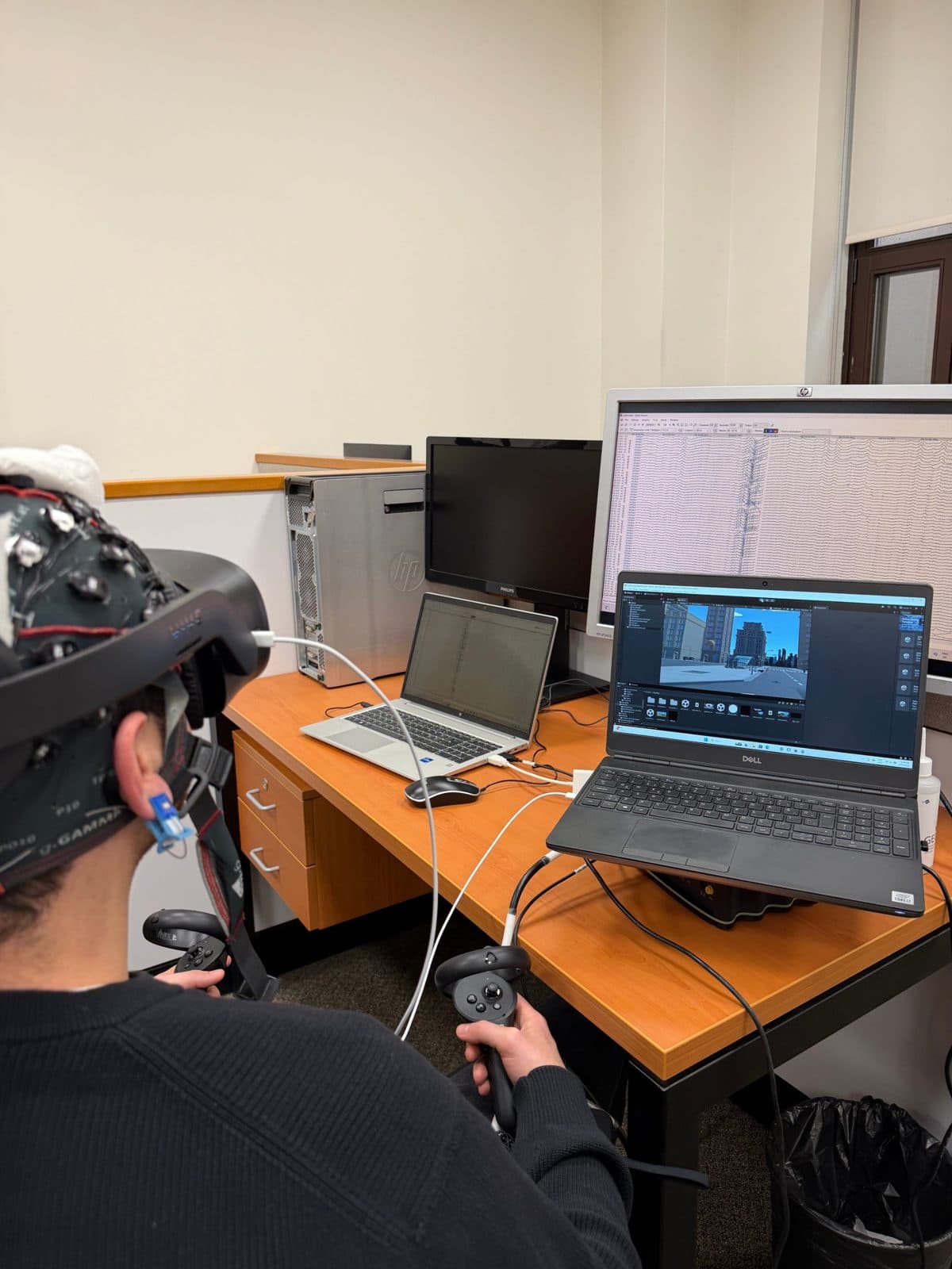 A participant wearing a VR headset over an EEG cap; a virtual city and EEG signals on the screens.