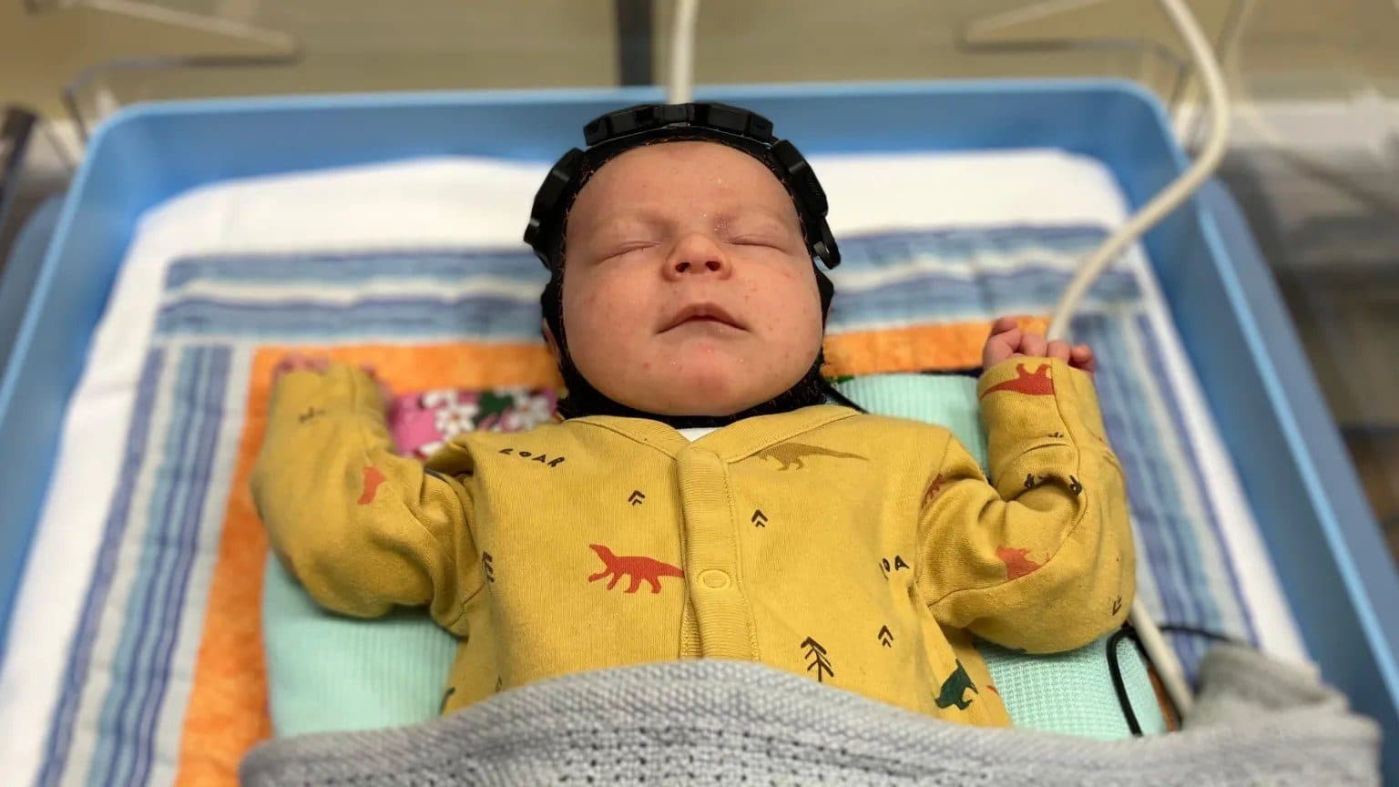 A newborn wearing a LUMO cap in a cot