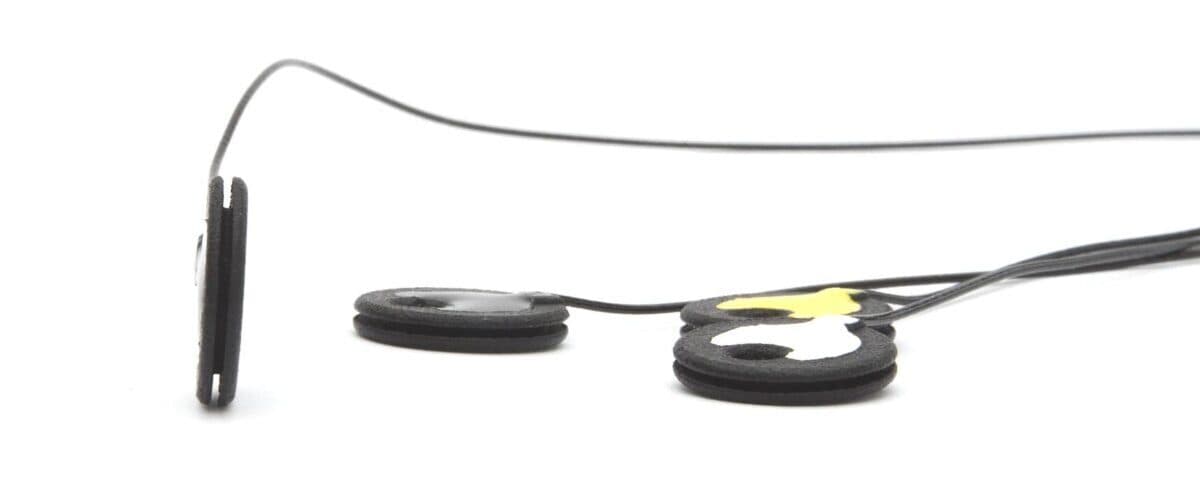 Three flat black g.Ladybird TMS-EEG electrodes with thin cables on a white background, one standing on its edge to show its thickness